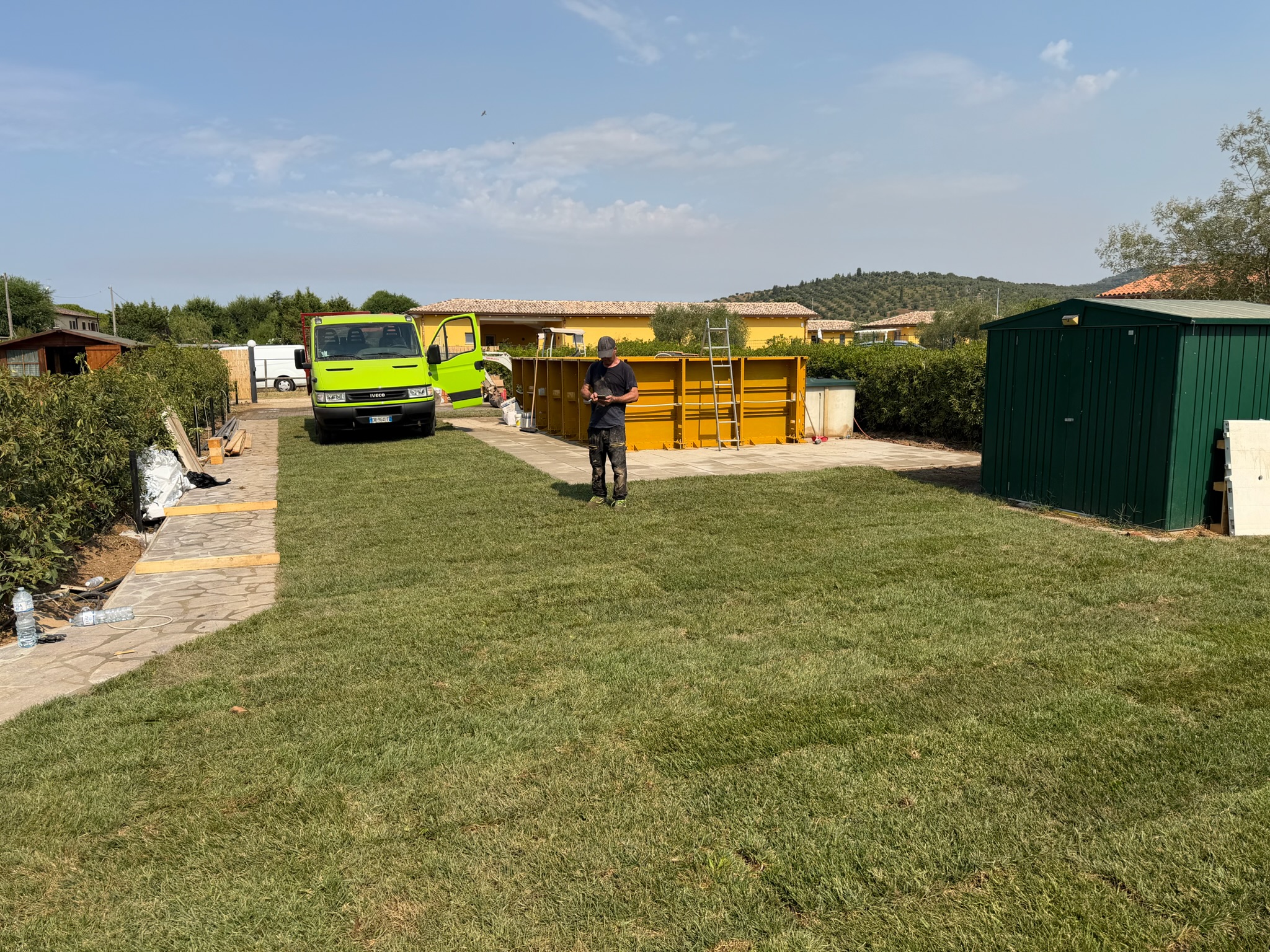 Prato e area verde durante le lavorazioni, con mezzi e attrezzature di cantiere sullo sfondo.