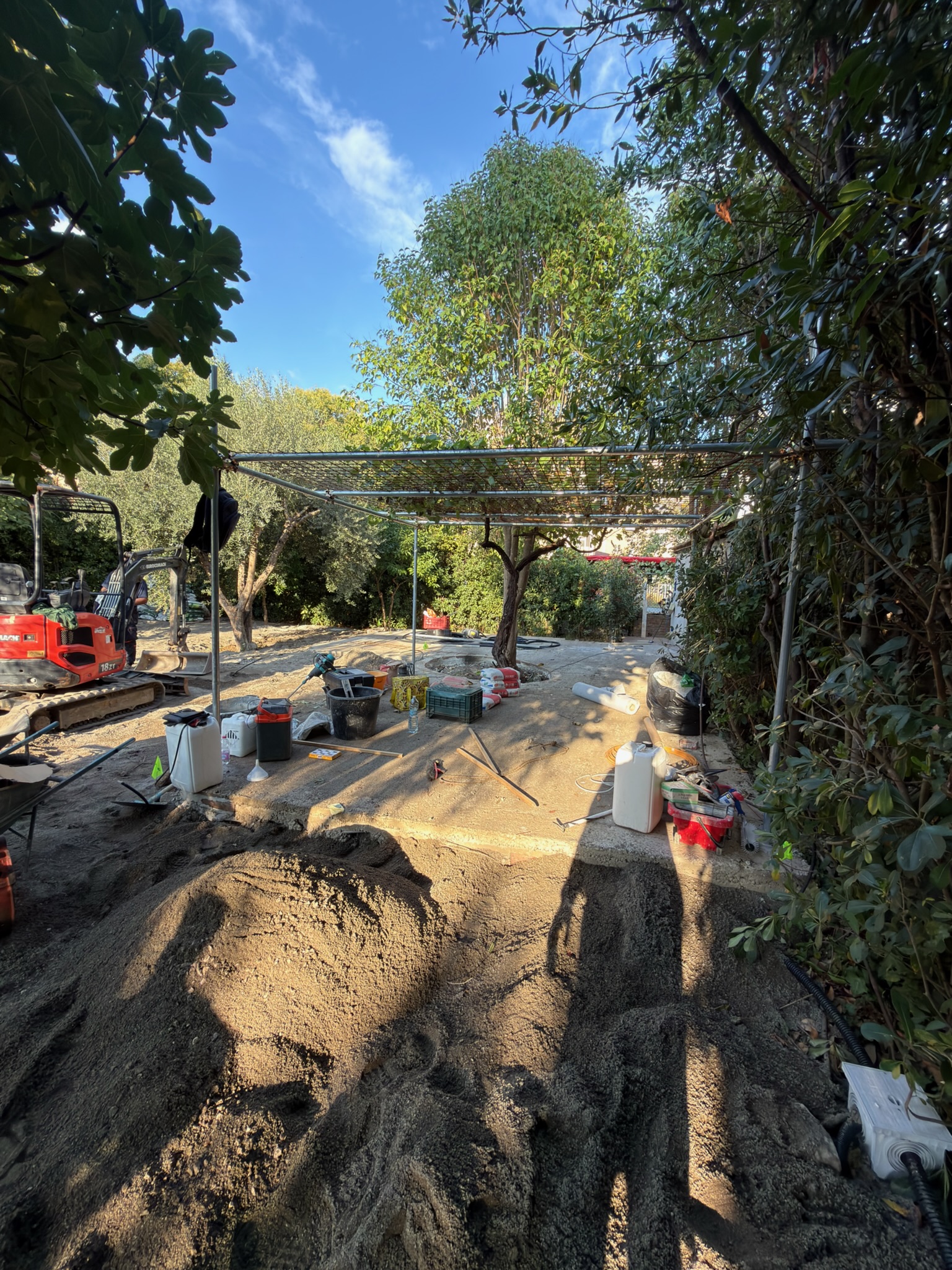 Realizzazione di un giardino con percorsi in ghiaia, bordature in laterizio e aiuole circolari integrate agli alberi esistenti.